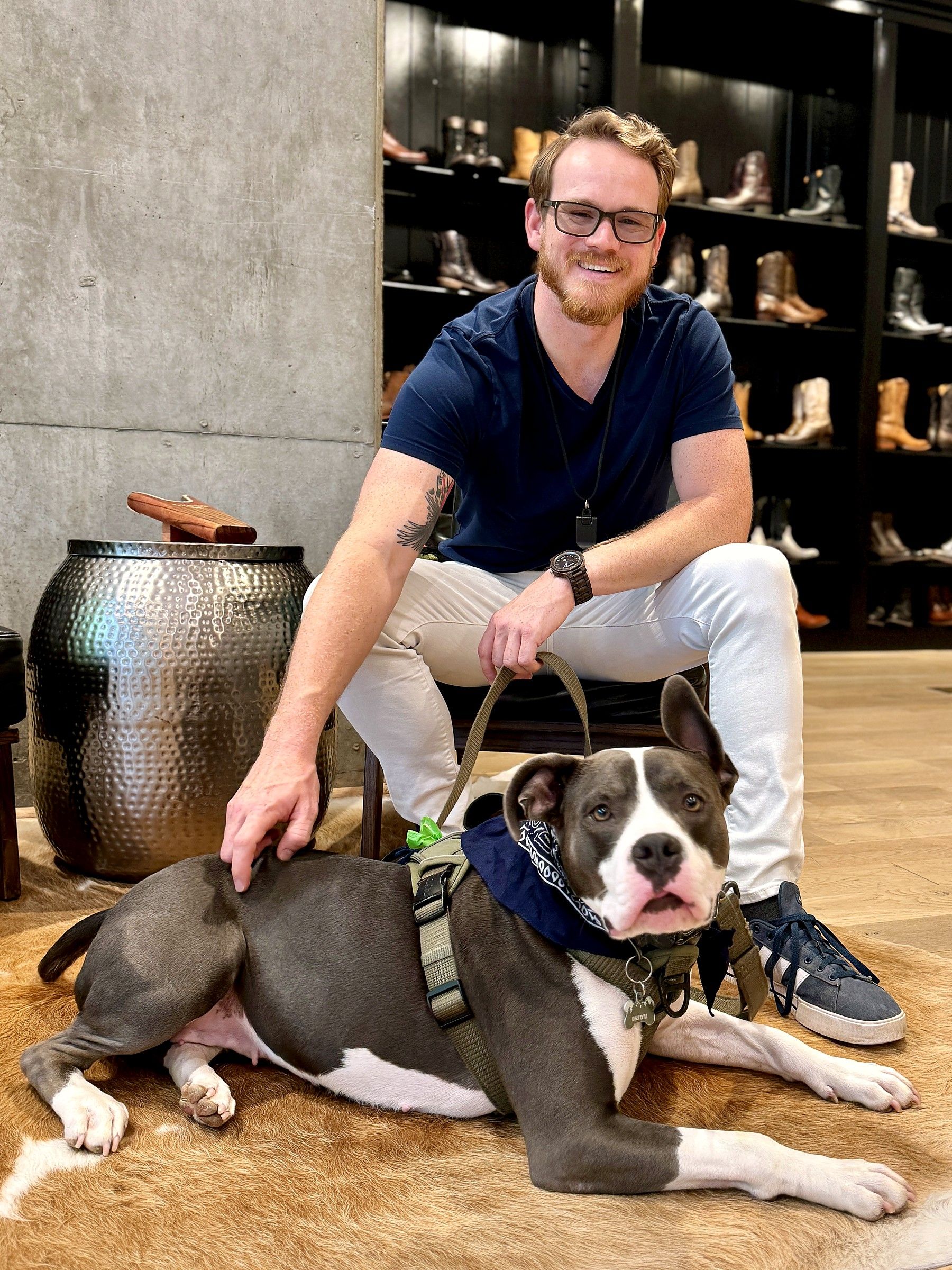 Phillip Greene seated indoors with his hand on Lucky, who is lying at his feet in a harness and bandana